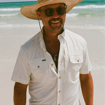 Man wearing The Key West white shirt with straw hat and sunglasses at the beach