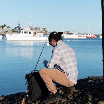man fishing on rocky beach in blue and orange flannel