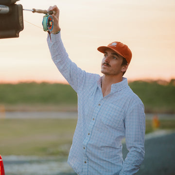 Man holding fly rod with blue grid long sleeve button down