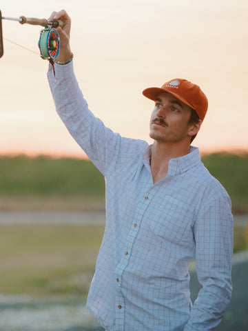 Man holding fly rod with blue grid long sleeve button down