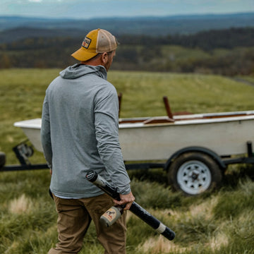can holding beverage and fishing rod case wearing grey hoodie