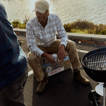 The Snowcat plaid shirt worn by a man seated beside a marina and barbecue grill