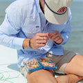 man tends to fly box while wearing a microcheckered blue and white performance western shirt with pearl snaps