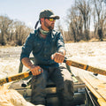 man rows canoe while wearing a deep blue long sleeve fishing performance shirt