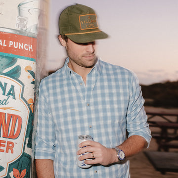Close up of man leaning on wall wearing blue plaid button down shirt
