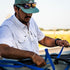 Man in a checked shirt and cap securing blue straps on an outdoor boat