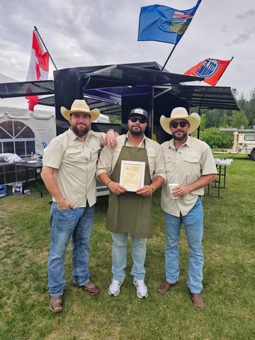 Three men in cowboy hats pose outdoors beside a tent while one holds a framed certificate.