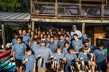 Group of people in gray shirts posing outdoors with a collection of freshly caught fish