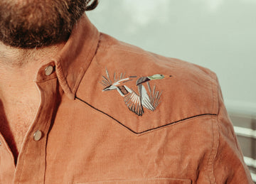 Close-up of a rust-colored shirt with embroidered bird detail on the chest and metal buttons