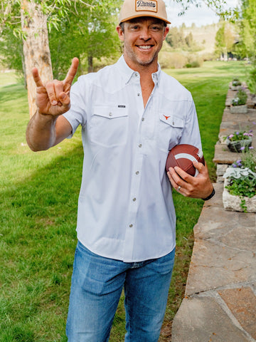 Smiling man in a light button shirt and cap holding a football in a leafy garden