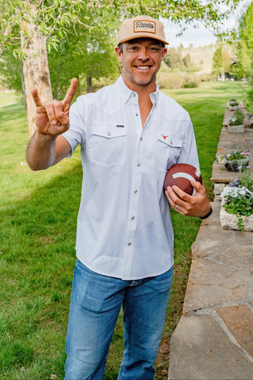Smiling man in a light button shirt and cap holding a football in a leafy garden