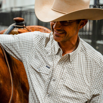 Man with his arm on a horse wearing plaid pearl snap shirt