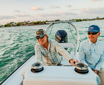 Two men in plaid shirts and sunglasses aboard a boat on sunny turquoise water