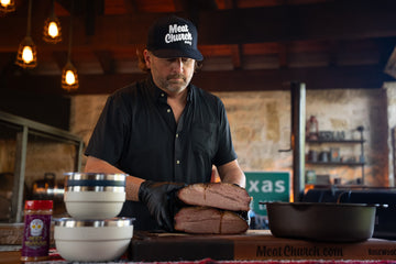 Man in a black shirt and cap prepares sliced meat on a cutting board in a rustic kitchen