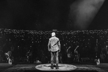 Black and white view of a performer in a shirt standing onstage before a crowd holding up lights
