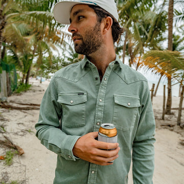 Man holding beverage on the beach with green denim shirt