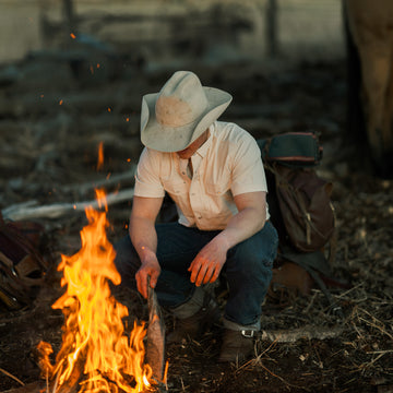 man tending fire in tan short sleeve shirt