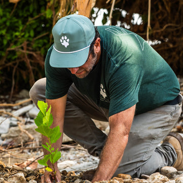 The Deep in the Heart Hat worn outdoors by a man planting a young tree beside a rocky stream