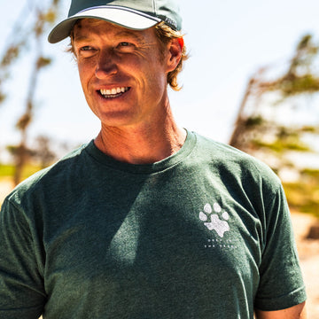 The Deep In The Heart T-Shirt featuring a paw print graphic worn by a smiling man outdoors