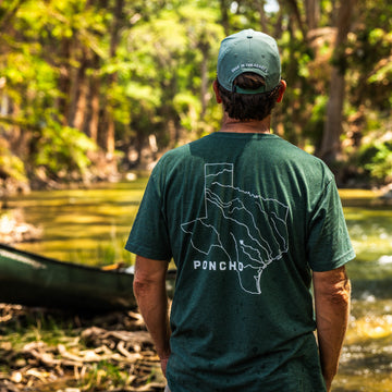 The Deep In The Heart T-Shirt with a Texas map graphic worn beside a wooded stream