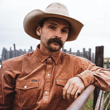 Cowboy wearing corduroy shirt leaning on a gate