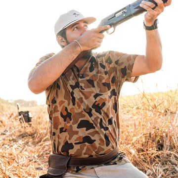 man shooting shotgun wearing camo polo shirt