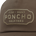 Close-up of brown fabric with an embroidered patch reading "Fish - Hunt Poncho Drifters" in beige thread.