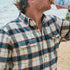man drinking beverage on the beach wearing half moon flannel