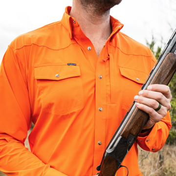 man holding shotgun wearing long sleeve blaze orange shirt
