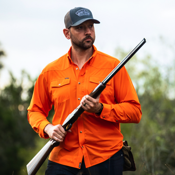 man holding shotgun wearing long sleeve blaze orange shirt