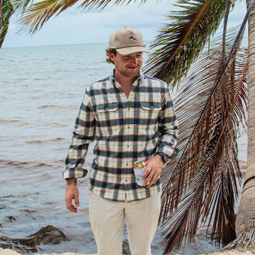 man holding beverage wearing the half moon flannel on the beach