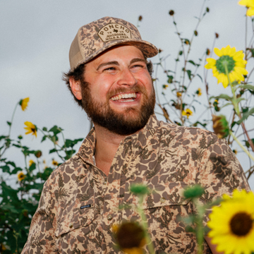 The Game Hat worn with a patterned shirt among blooming sunflowers outdoors