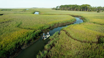 Aerial view of a small boat navigating a winding creek through a coastal marshland landscape