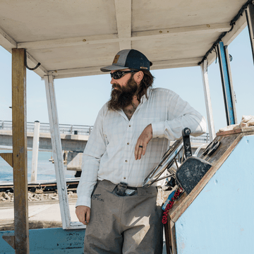 Man leaning on boat wearing green plaid button down shirt