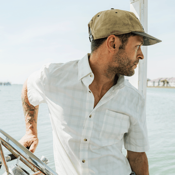 Man driving a boat wearing green plaid button down short sleeve shirt