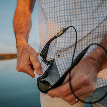 cleaning sunglasses in grey and blue plaid shirt