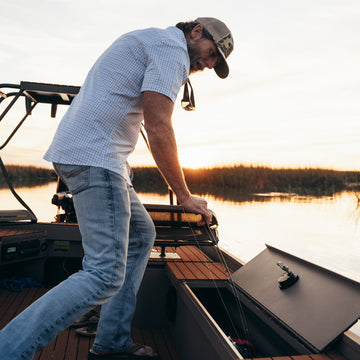 man in blue plaid putting away fishing pole in boat