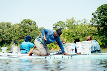 Men fishing from a boat on a sunny lake, with one man wearing a blue long-sleeve outdoor shirt