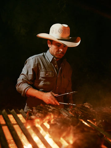 Cowboy grilling over a campfire at night in a western outdoor scene