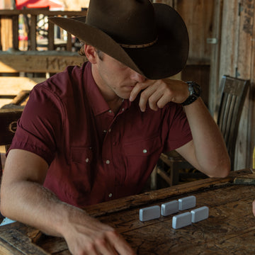 man playing dominos with maroon western short sleeve