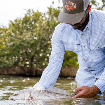 man holding redfish wearing long sleeve grey plaid shirt