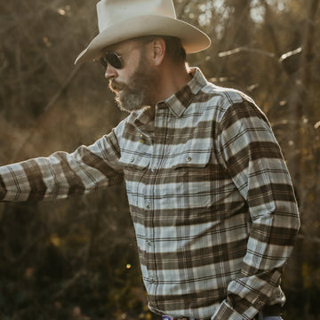 man walking through woods in blue and brown plaid flannel