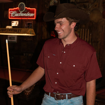 man holding pool cue in maroon short sleeve shirt