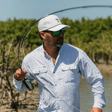 Man casting fly rod wearing white and blue button down shirt