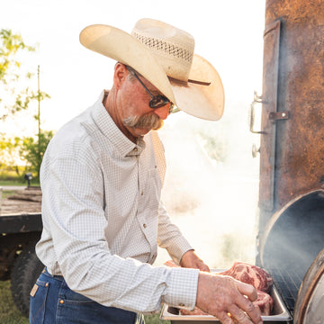 man cooking steaks in long sleeve grey and white plaid button up