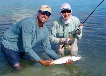 Two anglers wading in shallow water hold a fish beside a fishing rod outdoors