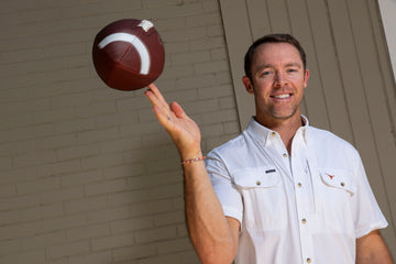 Man in a white short-sleeve shirt balancing a brown football on one finger