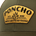 Close-up of an olive green hat with a stitched yellow patch reading "PONCHO EST. 2018 MADE FOR THE OUTDOORS" and a leaf logo.