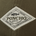 Close-up of a fabric patch on olive green material featuring "PONCHO" text, a fish graphic, and phrases about fishing shirts and outdoors.