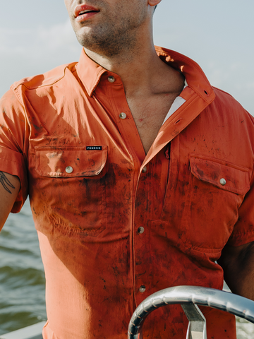 Orange men's outdoor button-down shirt with two flap chest pockets, worn on a boat over the water